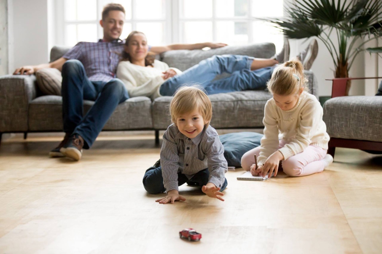 Parents sitting on the couch, watching as their children play in the hardwood floor living room at Window Accents & Flooring near Princeton, NJ