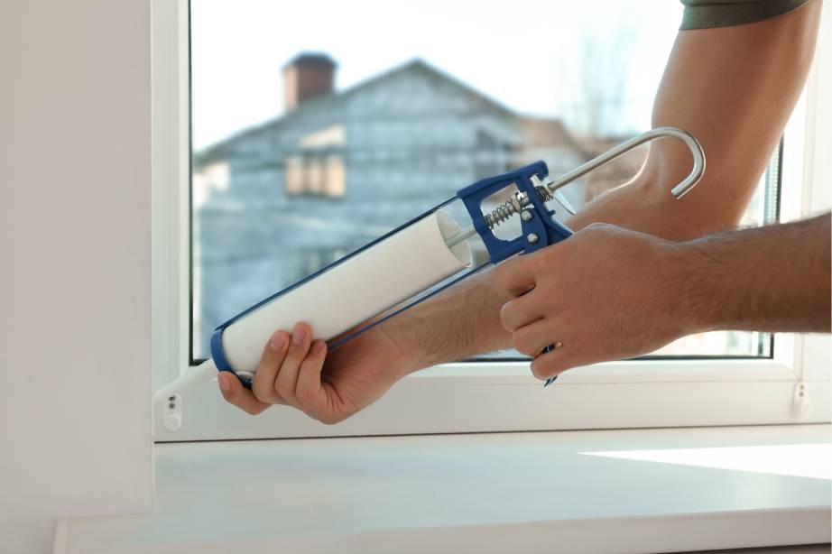 A person using caulk to prepare their windows for winter before adding Hunter Douglas cellular shades at Window Accents & Flooring near Princeton Borough, New Jersey (NJ)