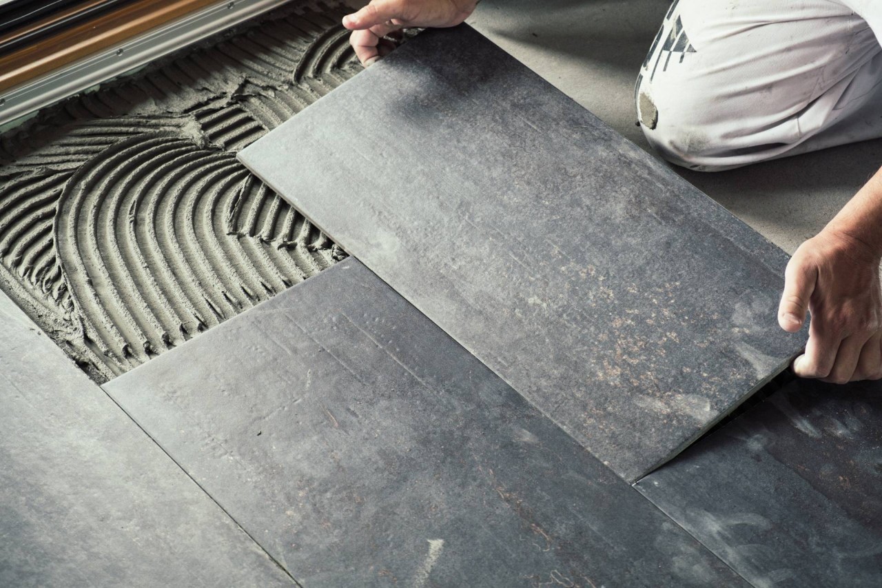 A professional flooring specialist installing dark ceramic tile flooring with adhesive in a residential home at Window Accents & Flooring near Princeton, New Jersey