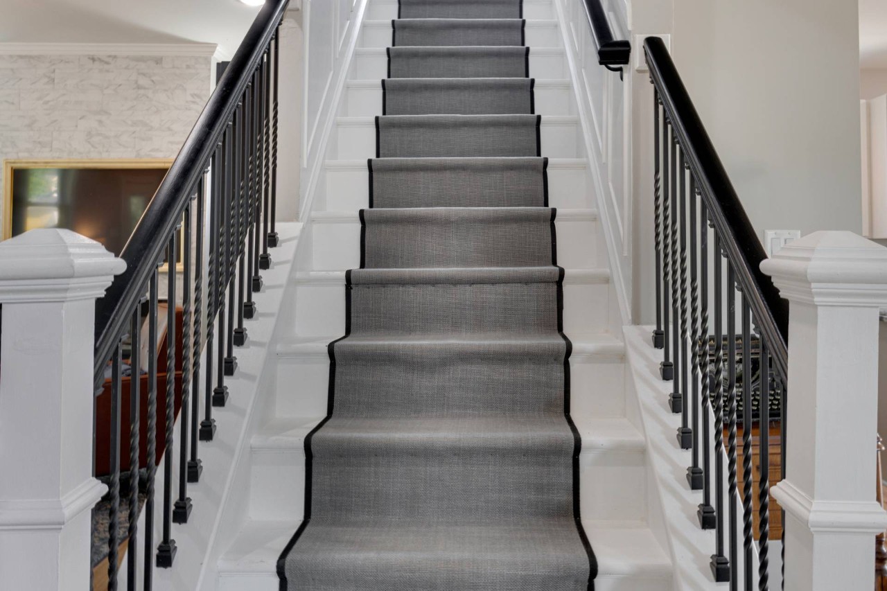 A large staircase with white steps, a modern stair runner, and sleek black railings at Window Accents & Flooring near Princeton New Jersey (NJ)